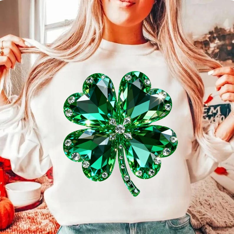 May include: White sweatshirt featuring a large, sparkling green four-leaf clover design. The clover is embellished with clear crystals around the edges and in the center, creating a dazzling effect. The design is centered on the front of the shirt.