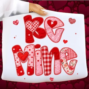 Könnte beinhalten: Ein weißes Kissen mit den Worten "Be Mine" aus applizierten roten, rosa und floralen Stoffen. Die Buchstaben sind im Patchwork-Stil gehalten, mit Herzakzenten und dekorativen Nähten. Das Kissen wird von einer Person gehalten.