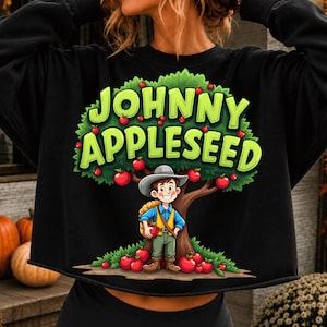 Puede incluir: Una sudadera negra de manga larga con un estampado gráfico de un personaje de dibujos animados con sombrero y un saco bajo un manzano. El texto JOHNNY APPLESEED está impreso en letras grandes de color verde claro.