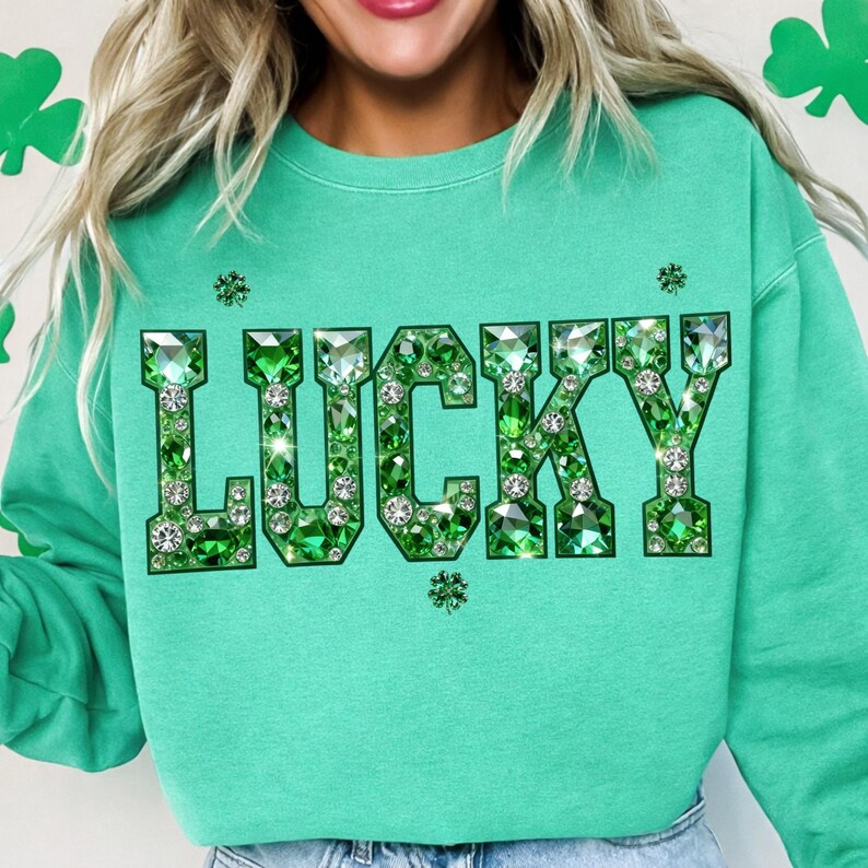 May include: A light green sweatshirt with the word "LUCKY" in large, sparkling green gem letters. The sweatshirt has a crew neck and long sleeves. Small gem accents are scattered around the word "LUCKY".