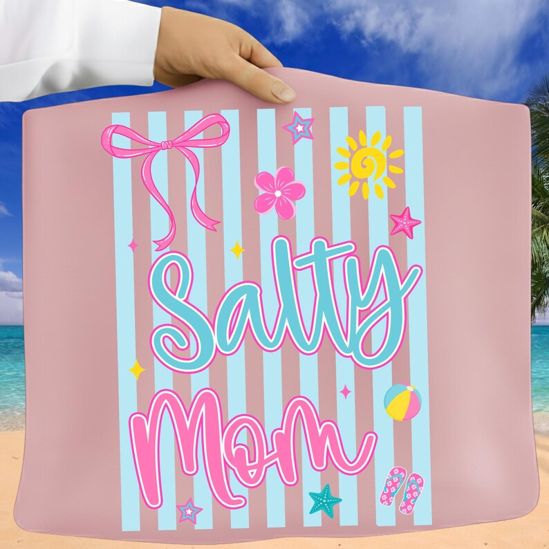 Pu&ograve; includere: Un telo da mare rosa con strisce verticali blu e le parole "Salty Mom" in turchese e rosa. Il telo presenta un fiocco, fiori, stelle, un sole, un pallone da spiaggia e infradito.