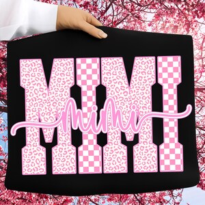 May include: Black tote bag featuring the word "MIMI" in large pink letters. The letters are a mix of leopard print and checkered patterns. The word "Mimi" is written in a cursive font across the letters.