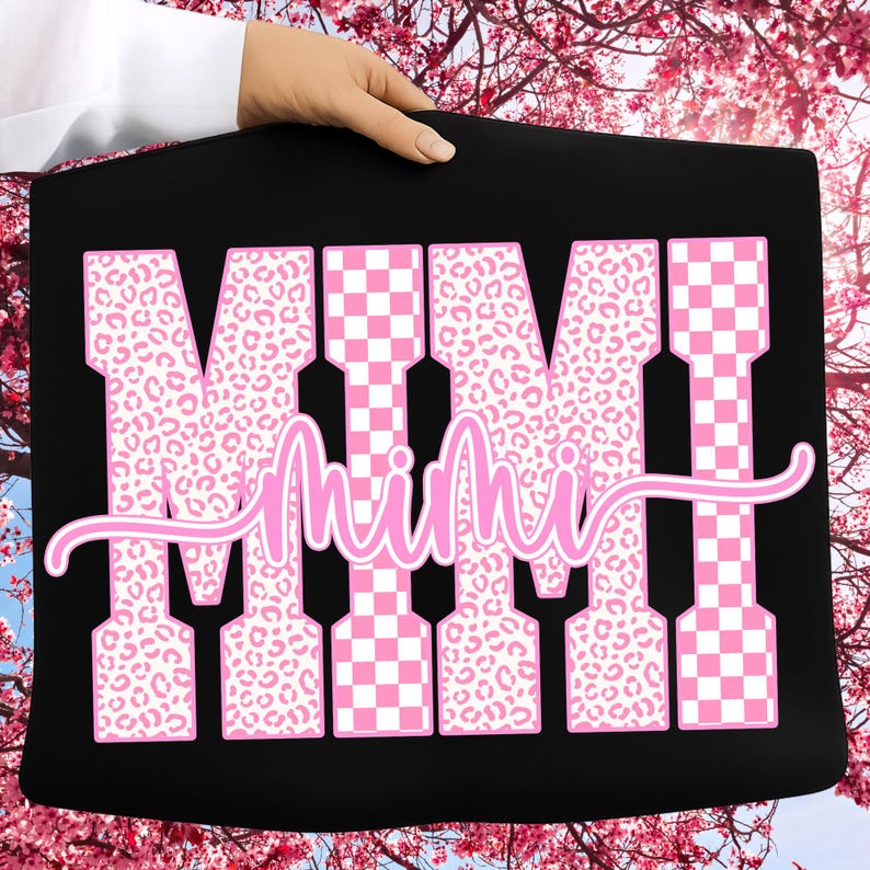 May include: Black tote bag featuring the word "MIMI" in large pink letters. The letters are a mix of leopard print and checkered patterns. The word "Mimi" is written in a cursive font across the letters.