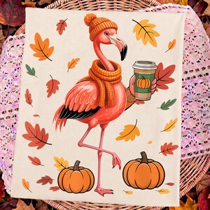 May include: A cream-coloured fabric featuring a pink flamingo wearing an orange knit beanie and scarf. The flamingo holds a coffee cup with a pumpkin graphic. Two orange pumpkins sit at the base, surrounded by scattered red, orange, and yellow leaves.