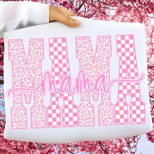 May include: A white rectangular sign with the word "MAMA" in pink. The letters alternate between a leopard print and a pink and white checkerboard pattern. The word "mama" is written in cursive below the word "MAMA".