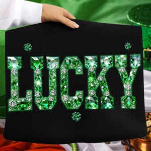 May include: Black sign with the word "LUCKY" spelled out in green gemstones and white rhinestones. The sign has a shamrock in each corner. The sign is held by a person.
