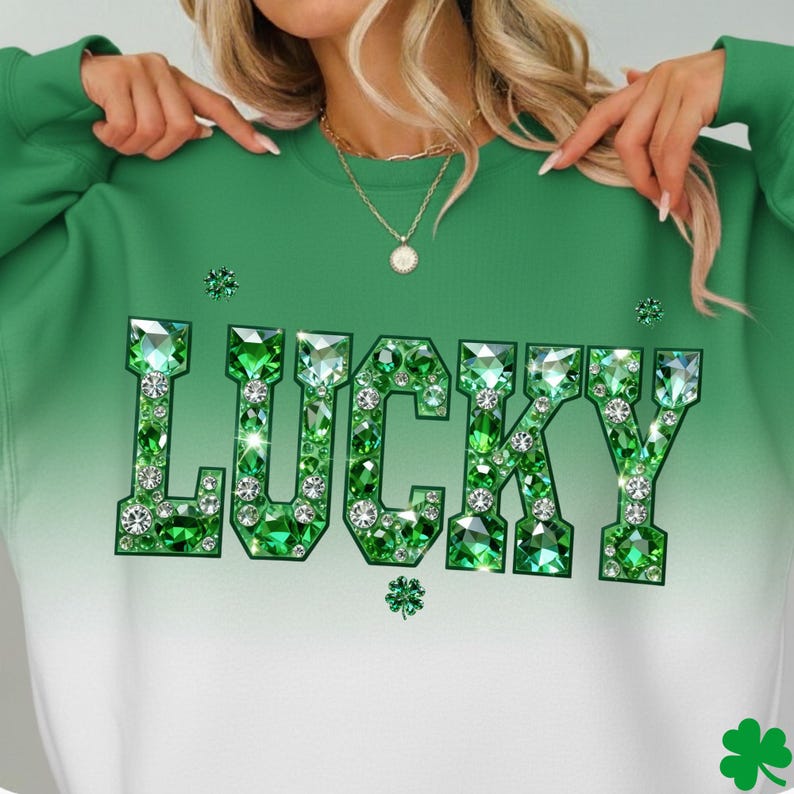 May include: Green sweatshirt with the word "LUCKY" in large, sparkling, emerald-colored letters. The letters are embellished with diamond-like accents. The sweatshirt has a gradient effect, transitioning from green at the top to white at the bottom. Shamrock details are also visible.