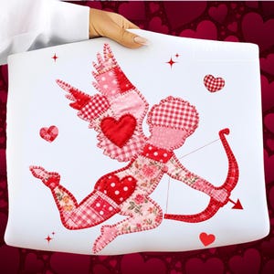 Puede incluir: Un cojín blanco con un diseño de patchwork que presenta a Cupido con arco y flecha. Cupido está hecho de telas rojas y rosas con patrones de corazón y cuadros. Corazones y estrellas decorativas están dispersos.