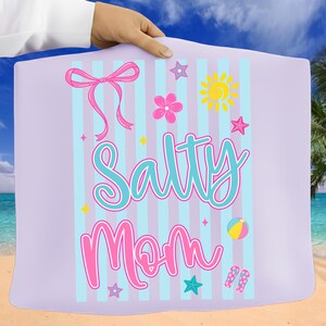 Pu&ograve; includere: Un telo da mare lilla chiaro con strisce blu verticali e le parole "Salty Mom" in corsivo turchese e rosa. L'asciugamano presenta un fiocco rosa, un fiore, un sole, stelle, un pallone da spiaggia e infradito.