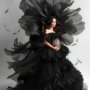 K&ouml;nnte beinhalten: Eine schwangere Person tr&auml;gt ein schwarzes T&uuml;llkleid mit einem gro&szlig;en, schwarzen, blumenf&ouml;rmigen Kopfschmuck. Das Kleid hat mehrere T&uuml;llschichten und der Kopfschmuck ist aus durchsichtigem Stoff.