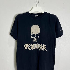 May include: Black t-shirt with a white skull graphic and Japanese text. The shirt has a crew neck and short sleeves. The word "CROWS" is printed on the collar.