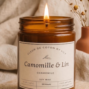 May include: A lit soy wax candle in an amber glass jar with a white label reading Fleur de Coton by Lily, Camomille & Lin, Chamomile, 8 oz / 227g, 50 hours, and 100% natural organic. The candle features a single flame and a simple botanical illustration.