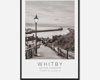 May include: A black and white photograph of a street in Whitby, England. The street is lined with houses and a lamppost. The street leads down to a harbor with a pier and a lighthouse in the distance. The text "WHITBY, UNITED KINGDOM, 54.4863° N / 0.6133° W" is printed below the image.