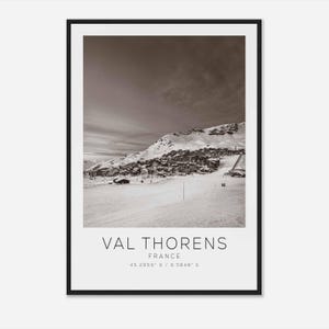 Könnte beinhalten: Ein Schwarzweißfoto einer schneebedeckten Bergkette mit einem Dorf, das sich im Tal befindet. Der Text "VAL THORENS FRANKREICH 45.2859° N / 6.5848° E" ist unter dem Bild gedruckt.