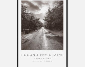 May include: Black and white photograph of a road winding through a forest, with the text "Pocono Mountains, United States" at the bottom. The sky is overcast, and the trees are bare. The coordinates are 41.0000° N / -75.5000° W.