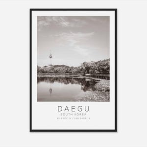 May include: A black and white photograph of a lake with a tower in the background. The text "DAEGU SOUTH KOREA 35.8501° N / 128.5206° E" is printed below the image.