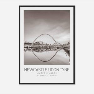 May include: A black and white photograph of the Tyne Bridge in Newcastle upon Tyne, United Kingdom. The bridge is a modern arch bridge with a distinctive curved design. The photo shows the bridge reflected in the water below.