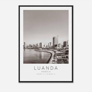 May include: A black and white photograph of Luanda, Angola. The photo shows a cityscape with buildings along a waterfront. The text "LUANDA ANGOLA 8.8147° S / 13.2302° E" is at the bottom of the image.