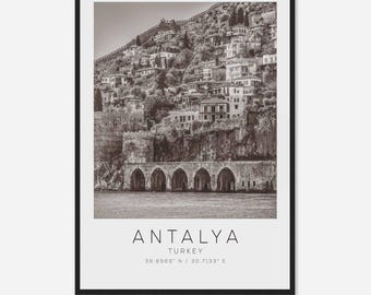 May include: A black and white photograph of Antalya, Turkey. The image shows a hillside with buildings and a bridge over the water. The text "ANTALYA TURKEY 36.8969° N / 30.7133° E" is printed below the image.