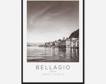 May include: A black and white photograph of the town of Bellagio, Italy, on Lake Como. The photo shows a row of buildings along the lakeshore with mountains in the background.