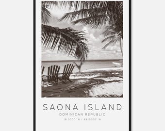May include: Black and white framed print of Saona Island in the Dominican Republic. The image features two wooden beach chairs on a sandy shore, palm trees, and the ocean. Text at the bottom reads "SAONA ISLAND, DOMINICAN REPUBLIC, 18.0000° N / 69.6000° W."