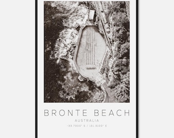 May include: Monochrome framed print depicting Bronte Beach in Australia from above. The image shows a swimming pool built into the cliffs, with the sea waves visible. The text "BRONTE BEACH AUSTRALIA" and coordinates are printed at the bottom.