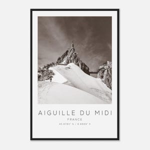 Peut inclure: Photographie en noir et blanc de l'Aiguille du Midi en France, avec un paysage enneigé et une structure au sommet. L'image comprend le texte "AIGUILLE DU MIDI FRANCE 45.8780° N / 6.8899° E". La photographie est encadrée d'un bord noir.