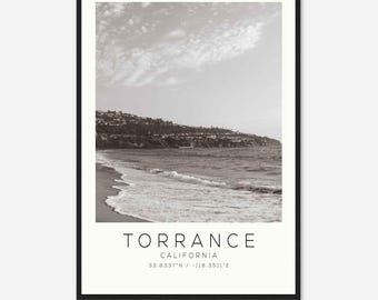 Pode incluir: Uma fotografia a preto e branco de uma praia em Torrance, Califórnia. A foto mostra uma praia de areia com ondas a quebrar na costa. O nome da cidade "Torrance" e as coordenadas "33.8337°N / 118.3511°E" estão impressas abaixo da imagem.