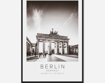 May include: A black and white photograph of the Brandenburg Gate in Berlin, Germany. The gate is a large, neoclassical structure with five archways and a quadriga statue on top. The photo was taken from a distance, showing the gate in its entirety.