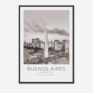 Puede incluir: Una fotografía en blanco y negro del Obelisco en Buenos Aires, Argentina. El obelisco es un monumento alto y delgado que se encuentra en medio de una intersección concurrida. La foto muestra el obelisco rodeado de edificios y tráfico.