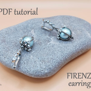 Puede incluir: Un par de pendientes de plata con una perla azul claro y detalles de cristal. Los pendientes están sobre una piedra gris con el texto "FIRENZE earrings" y "PDF tutorial" en la imagen.