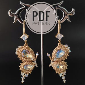 May include: Gold-toned beaded butterfly earrings with iridescent crystals and square-cut clear crystals. The earrings are displayed on a silver stand against a black background. The text "PDF PATTERN" is in a white circle.