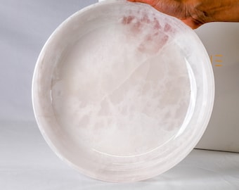 May include: A large, round, white serving dish made of natural alabaster with a subtle pink hue. The dish has a smooth, polished surface and a slightly raised rim.