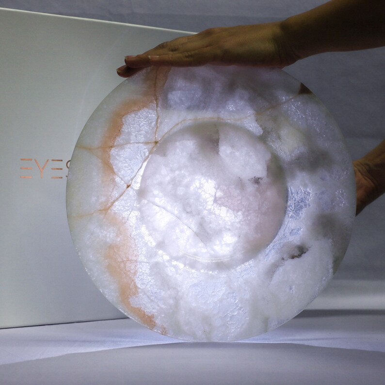 Pode incluir: Uma tigela de alabastro branco com um padr&atilde;o delicado e intrincado de veios e redemoinhos. A tigela tem uma superf&iacute;cie lisa e polida e uma forma ligeiramente arredondada.