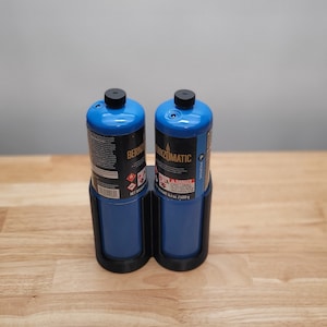 May include: Two blue propane canisters in a black holder. The canisters are labeled "Bernzomatic" and have a warning label that says "Danger".