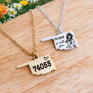 May include: Two necklaces with pendants shaped like the state of Oklahoma. One is gold-toned with the zip code 74055 and a heart. The other is silver-toned with the text "HOME is with you" and a picture of a couple.