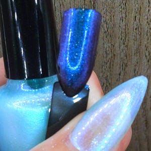 May include: A bottle of iridescent nail polish with a black cap is next to a painted nail. The nail is painted with a blue and purple color-shifting polish. Another nail is painted with a light blue iridescent polish.