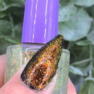 May include: A close-up of a nail with a dark base and a shimmering, multi-colored glitter top coat. The nail is held near a bottle of nail polish with a purple cap. The nail polish bottle is clear with a glittery, iridescent finish.