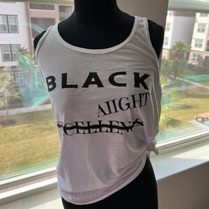May include: White tank top with black text that reads "BLACK AIGHT" and "CHILLEN".