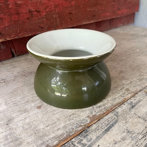 May include: A ceramic bowl with a wide, flared rim and a rounded base. The exterior of the bowl features a glossy olive green glaze, while the interior and the top surface of the rim are finished in a smooth, off-white, cream-colored glaze.