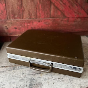 May include: A brown vintage briefcase with a silver handle and trim. The briefcase has a rectangular shape and a secure locking mechanism. The case is closed and appears to be made of a durable material, suitable for carrying documents or small items.