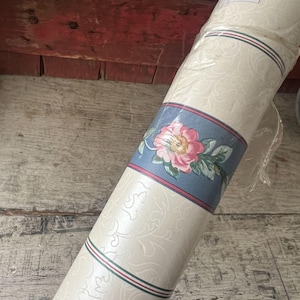 May include: Rolled wallpaper featuring a floral design with a blue border. The border has a pink and green stripe. The wallpaper has a cream background with a subtle embossed pattern. The floral design includes a pink rose.