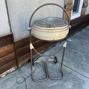 Pu&ograve; includere: Un ventilatore oscillante vintage beige e marrone, con una gabbia circolare e un manico curvo. Il ventilatore &egrave; montato su un supporto in metallo marrone con ruote. Il design &egrave; retr&ograve;, combinando funzionalit&agrave; con un'estetica classica.