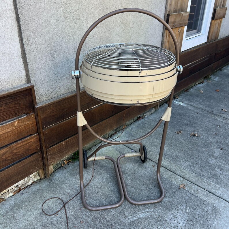 Pu&ograve; includere: Un ventilatore oscillante vintage beige e marrone, con una gabbia circolare e un manico curvo. Il ventilatore &egrave; montato su un supporto in metallo marrone con ruote. Il design &egrave; retr&ograve;, combinando funzionalit&agrave; con un'estetica classica.