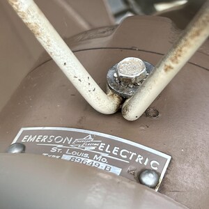 May include: Close-up of an Emerson Electric label on a brown appliance. The label reads "EMERSON ELECTRIC St. Louis, Mo. TYPE 89649-B". A metal bolt and a white wire are also visible.