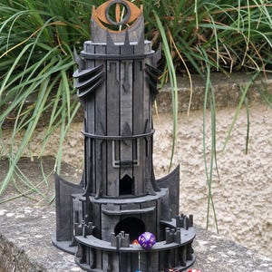 May include: A black wooden tower with a large eye symbol on top. The tower has a circular base with a small opening in the center. There are several colorful dice scattered around the base of the tower.