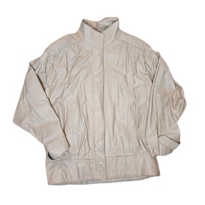 May include: A cream-colored leather jacket with a stand-up collar, a zipper closure, and two pockets. The jacket has a slightly puffed sleeve design.