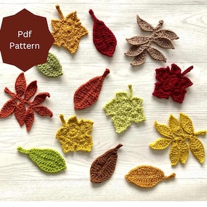 Puede incluir: Una colección de 12 hojas de ganchillo en varios colores, incluyendo rojo, naranja, amarillo, verde y marrón. Las hojas están dispuestas sobre una superficie de madera clara. Pdf Pattern.