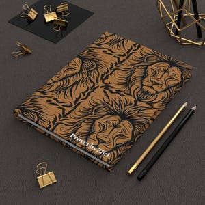 May include: A brown journal with a black lion design and the text "Proverbs 28:1". The journal is surrounded by gold and black office supplies, including paper clips and pencils. The journal is closed.