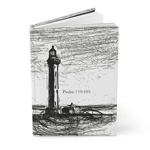 May include: A hardcover journal with a black and white sketch of a lighthouse. The cover features the text "Psalm 119:105" in a simple font. The journal is open, revealing blank white pages.